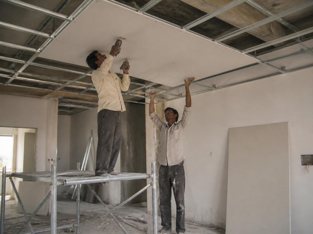 Workers installing a gypsum false ceiling on metal furring on a BRYX site